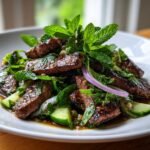 Close-up of juicy grilled steak slices mixed with fresh mint, cucumbers, and red onion in a Thai Beef Salad.
