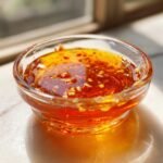 Close-up of a small glass bowl filled with vibrant, glossy Thai Dipping Sauce featuring chili flakes and minced garlic.
