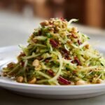 Close-up of a mound of shredded green papaya or mango, resembling Thai Mango Salad, topped with peanuts and chili flakes.