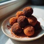 A stack of rich, dark Tiramisu Truffles heavily dusted with cocoa powder, sitting on a light ceramic plate.