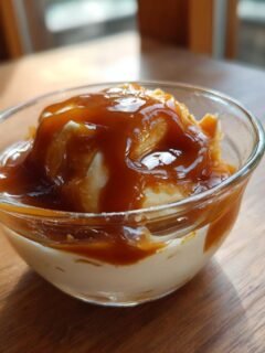 A small glass bowl containing a scoop of light-colored dessert topped generously with glossy Vegan Caramel Sauce.
