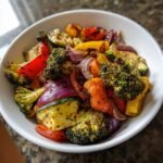 Close-up of a white bowl filled with colorful Whole30 Sheet Pan Roasted Vegetables, including broccoli, red onion, and peppers.